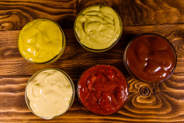 Different sauces in glass bowls on wooden table. Top view