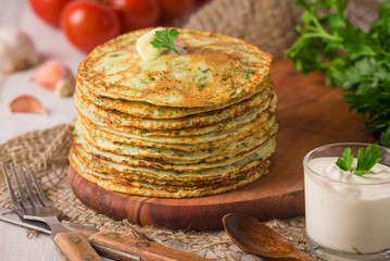 Many pancakes with fresh herbs and sour cream sauce on a wooden table. Traditional Ukrainian or Russian pancakes. Traditional dishes on the holiday Carnival Maslenitsa Shrovetide. Rustic style