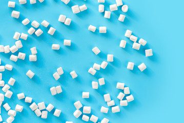 Marshmallows on blue background with copyspace. Flat lay or top view. Background or texture of colorful mini marshmallows. Winter food background concept.