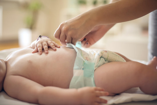 Young mother with her little baby boy at home changing diapers. Close up.