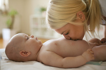 Young mother at home kissing her nicked little baby on bed.