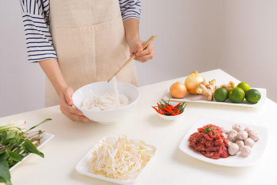Female chef prepare traditional Vietnamese soup Pho bo with herbs, meat, rice noodles