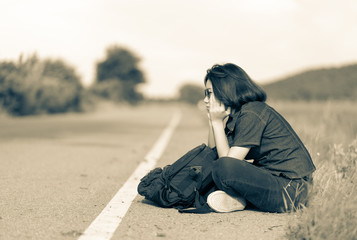 Woman sit with backpack hitchhiking along a road in countryside