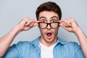 Close up portrait of astonished, shocked, attractive guy holding eyelets of glasses on his face...