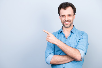 Portrait of handsome confident expert qualified smart with toothy beaming smile wearing denim shirt with rolled-up sleeves pointing with forefinger on empty blank copyspace isolated on gray background