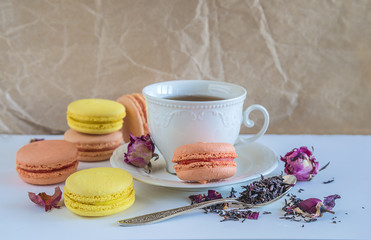 French macaroons and cup of black tea with rose petals on crumpled paper background