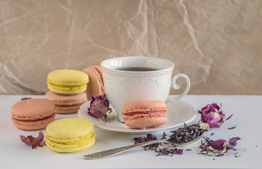 Tea time with french macaroons and cup of black tea with rose petals on crumpled paper background