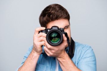 Portrait of guy in jeans shirt looking at photo camera, shooting photographs during excursion, making photosession over gray background