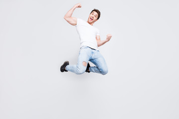 Full-size full-length portrait of carefree restless cheerful joyful stylish trendy guy with modern haircut dressed in denim trousers boots white t-shirt raising fists isolated on gray background