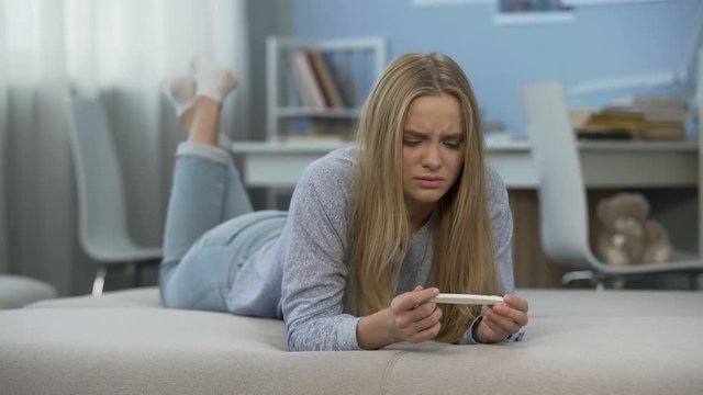 Teen girl sees two strips on pregnancy test, crying, feels desperate and fear