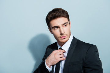 Close up portrait of handsome cool posh attractive confident serious with modern hairdo employee touching correcting tie with hand isolated on gray background copy-space