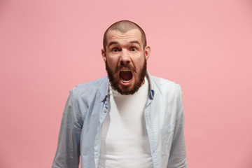 The young emotional angry man screaming on pink studio background