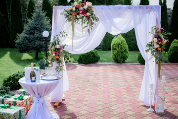 Wedding altar made of white cloth put on the frame and colorful bouquets stands on the sunny backyard
