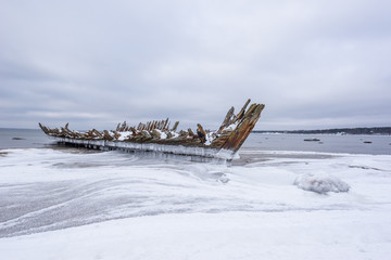 Old broken boat wreck and rocky beach in wintertime. Frozen sea, evening light and icy weather on...