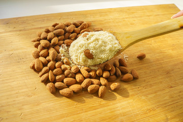 Almond flour in a wooden spoon on a background of nuts almonds.