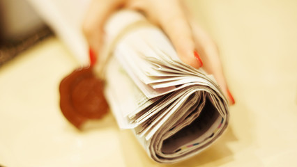 Newspaper in the hand. Folded daily papers with news tied with rope and seal. Young woman with red nails holding fresh tabloid pages with headlines and articles sealed with wax stamp. Close up