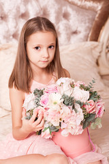 Cute kid girl 4-5 year old holding flowers sitting in bed close up. Looking at camera. Childhood.