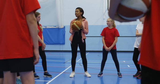 4K Sports teacher with young pupils on school basketball court, giving instruction how to play the game
