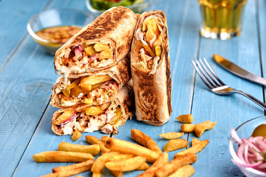 Shawarma chicken roll in a pita with fresh vegetables, cream sauce and french fries on wooden background. Selective focus