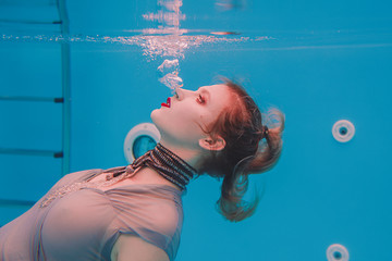 Amazing beautiful art surreal portrait of young woman in grey dress and beaded scarf underwater in the swimming pool