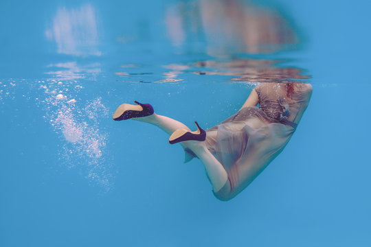 Amazing beautiful art surreal portrait of woman's legs in violet shoes underwater in the swimming pool