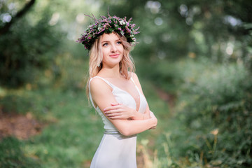 Bride in light white dress stands in wreath in the forest