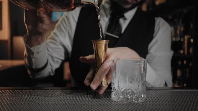 Cinemagraph of professional bartender at nigh club or bar at restaurant, pour liquor or alcohol into jigger measuring glass, when prepares cocktail for customer