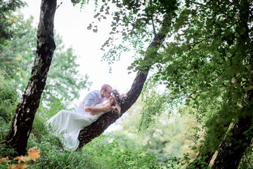 Adorable bride and groom lie on the tree in a green summer forest