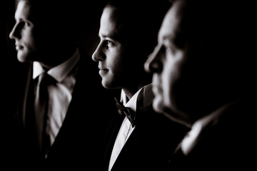 Profiles of three men in festive suits standing in the room
