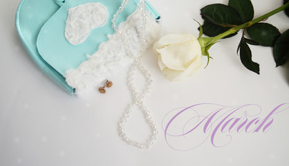 white rose, green earrings and turquoise bag on a white background  inscription 