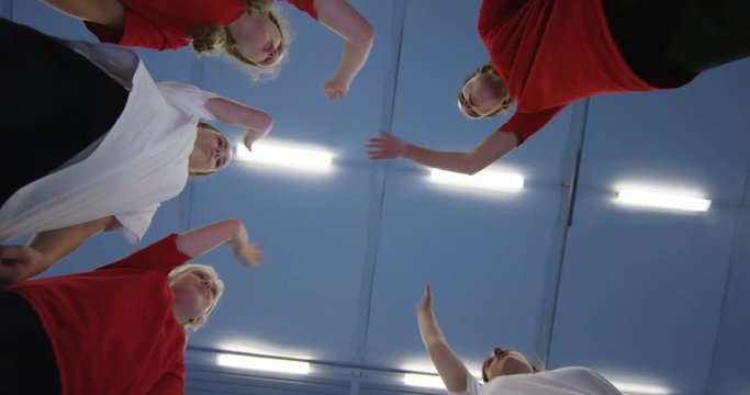 4K Low angle view looking up, young girls standing in a circle in school gym put hands together before sports game