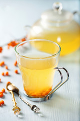 Vitaminic healthy sea buckthorn tea in small glass tea pot with fresh raw sea buckthorn berries. Selective focus