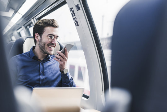 Happy businessman in train using cell phone