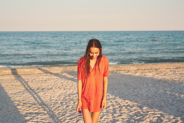 beautiful young woman in mans red polo walking along the beach against the sea and sky. happy woman enjoying summer vacation