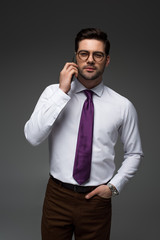 Smiling businessman in glasses talking on smartphone isolated on grey