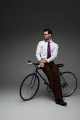 Image of  stylish businessman sitting on bicycle on grey