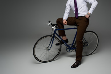 Cropped view of businessman sitting on bicycle on grey