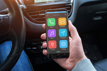 Smart car app in driver hand on modern smart phone with round edges. Car interior in background.