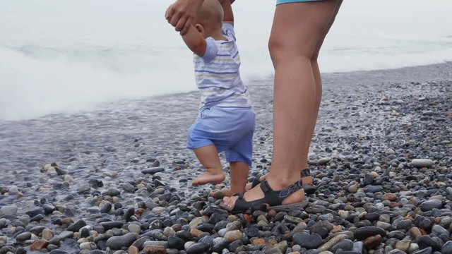 A little baby boy is playing and walking with his mother on the beach