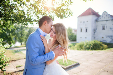 Groom holds bride tender posing with her before an old castle in a sunny summer day
