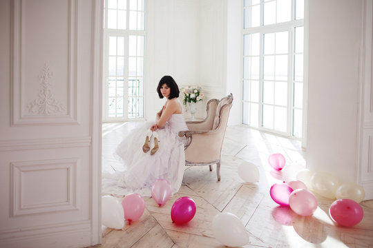 Young woman in wedding dress in luxury interior with a mass of pink and white balloons.