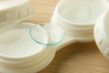 Contact lenses for the eyes and a white container with a solution on a wooden table