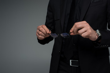 Partial view of male hands holding glasses isolated on grey