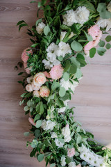 Green wreath with leaves and white flowers hangs on the wooden wall as part of wedding decor