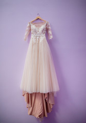 Wedding dress in color of dusty rose hangs on violet wall