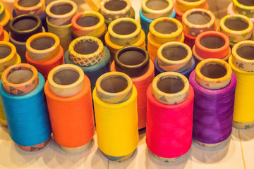 Background with a lot of colorful coils with threads. Bobbins are stacked in three rows, one on the other. The winding is erratic. Multicolored threads