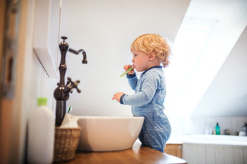 Cute toddler boy brushing his teeth in the bathroom.