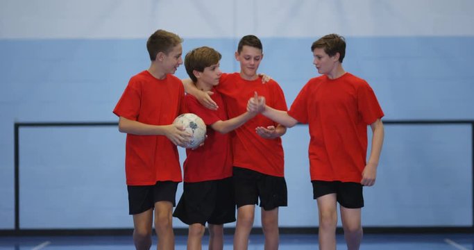 4K Happy confident young soccer team on indoor pitch walking together & giving high fives