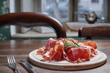 Wooden cutting board with prosciutto cheese on wooden table background.
