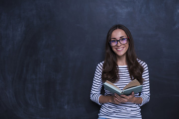Study concept. Beautiful smiling woman with book on blackboard background